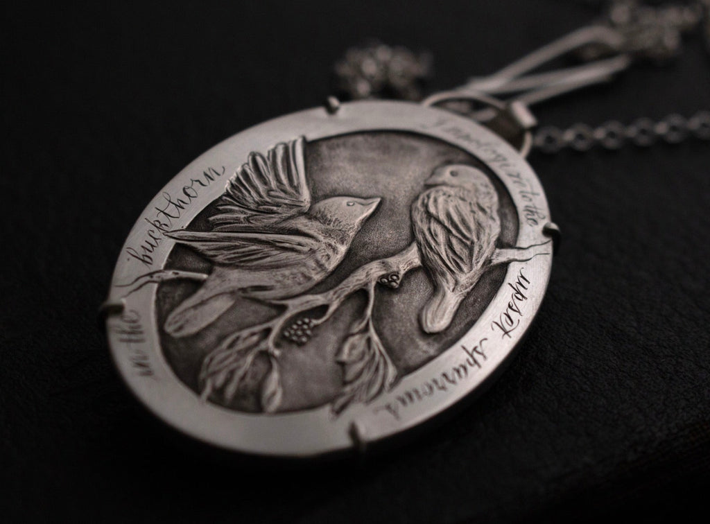 Hand engraved sterling silver pendant necklace featuring two sparrows in a buckthorn tree, displayed on a long chain with a clasp.